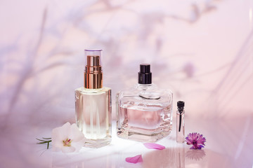 Different perfume bottles and sampler with plants on a pink floral background. Selective focus....