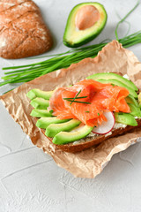 sandwich with avocado and salmon on a light background, green onions and gluten-free grain bread, radishes and tomatoes. concept diet food, copy space, sandwich take away, healthy fast food