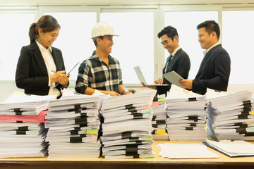 Pile of paperwork on table with group of happy business people standing.