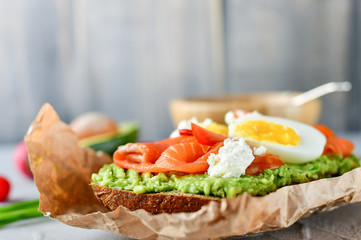 sandwich with avocado and salmon on a light background, green onions and gluten-free grain bread, radishes and tomatoes. concept diet food, copy space, sandwich take away, healthy fast food