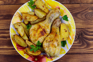 Baked chicken drumsticks with potatoes in a plate on wooden table