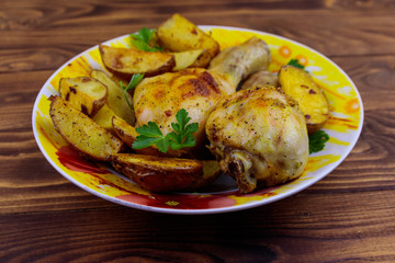 Baked chicken drumsticks with potatoes in a plate on wooden table