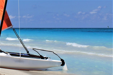 Catamaran on the beach, Varadero, Cuba. Partial view of a white catamaran with an orange sail,...