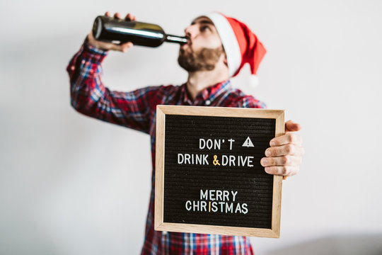 .Young man disguised as Santa Claus, drinking wine clearly drunk with a serious message on his blackboard "Don't drink and drive, Merry Christmas". Serious message.
