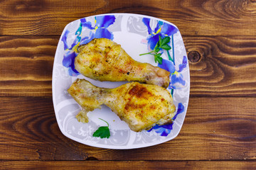 Baked chicken drumsticks with potatoes in a plate on wooden table