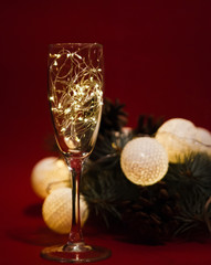 Wineglass with a christmas garland on red background with pine branches.
