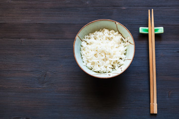 boiled rice in cup and chopsticks on rest on dark