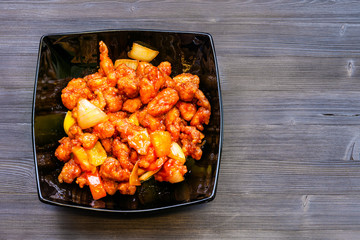 Sweet and Sour Chicken in black bowl on dark table