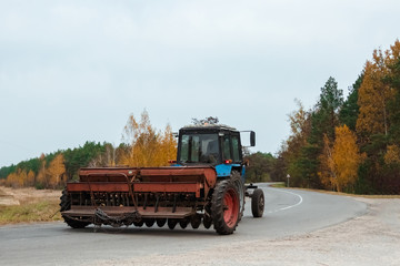 Fototapeta premium A blue tractor with a trailer for agricultural works rides along a road in a wheat field.