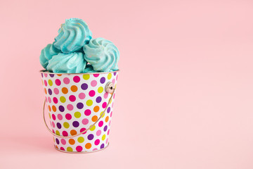 Small colorful bucket filled with blue meringue on a pink pastel background. Minimal concept with copy space.
