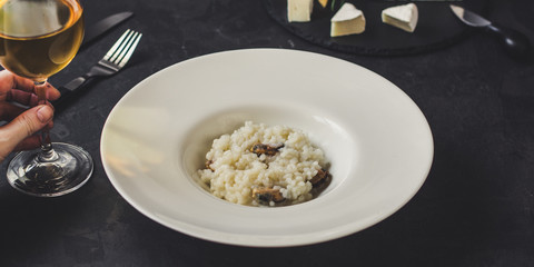 risotto with mussels (seafood rice) in a white plate and a glass of white wine on a dark background