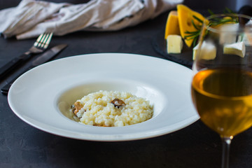 risotto with mussels (seafood rice) in a white plate and a glass of white wine on a dark background