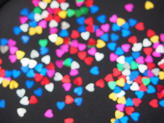Colorful shiny hearts lie on a black background. Hearts are blurry.