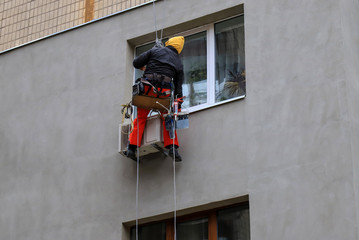 Industrial climber finishes the wall of the building after isolation. A man hangs on the ropes on the facade of a skyscraper