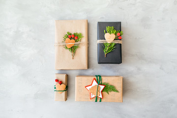 Wrapping Christmas gifts in recycled paper in rustic style. Xmas Gift boxes with craft paper, twine, coniferous branches, red berries and scissors on grey concrete background. Christmas gift pack