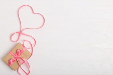 A gift of craft paper and a pink ribbon on a white wooden table. Place for text, copy space, Valentine's day postcard.