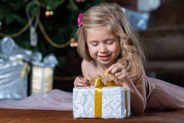 Little smiling girl opens a gift box on the floor next to the Christmas tree