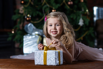 Little smiling girl with Christmas gift box lying on the floor on Christmas tree background