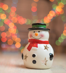 Ornamental snowman candle light holder  against a background of colorful Christmas holiday lights.