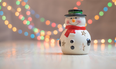 Ornamental snowman candle light holder  against a background of colorful holiday lights with free space for text .
