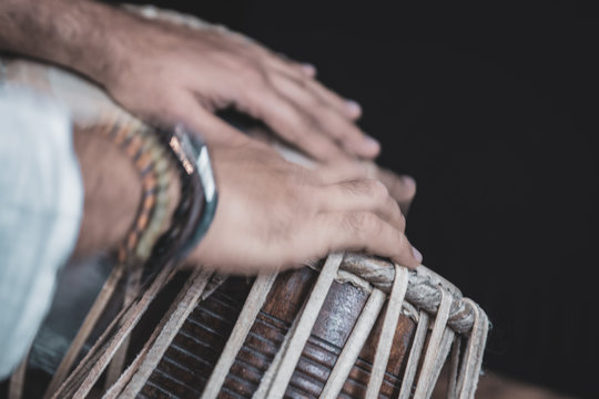 Images of a man's hands (wearing beads) playing the Tabla - Indian classical music percussion instrument - black background.