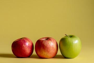 Two red and one green apple on a yellow background.