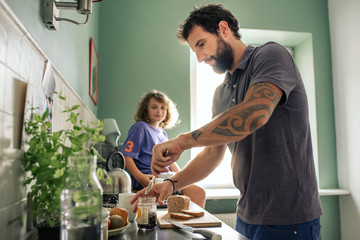 Young boy watching his father make sandwiches in their kitchen