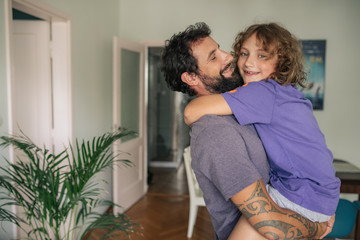 Smiling boy being held by his dad at home