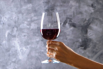 Close up of female arms swirling wineglass with expensive pinot noir wine in one hand against light grunged concrete wall background. Cropped shot, copy space for text.