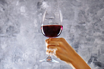 Close up of female arms swirling wineglass with expensive pinot noir wine in one hand against light grunged concrete wall background. Cropped shot, copy space for text.
