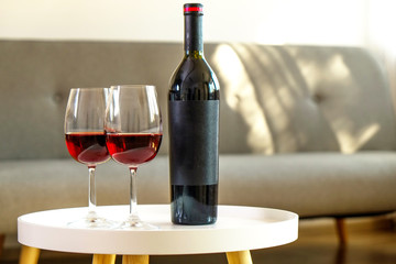 Vintage bottle of red wine with blank matte black label on table with two glasses in empty loft living room. Expensive bottle of cabernet sauvignon concept. Copy space, top view, close up.