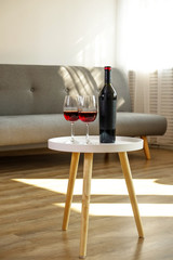Vintage bottle of red wine with blank matte black label on table with two glasses in empty loft...