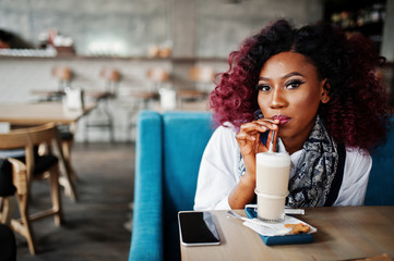 Attractive african american curly girl sitting at cafe drinking latte.