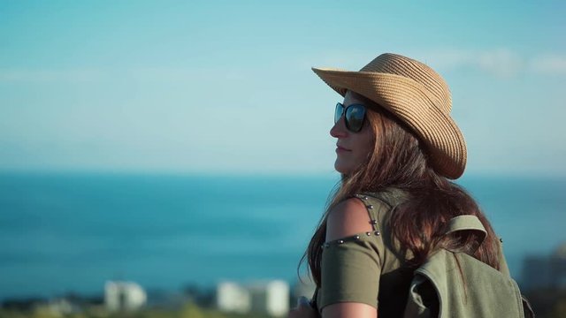 Smiling successful backpacker woman admiring amazing seascape on peak of mountain