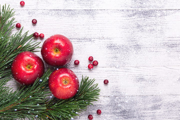 Christmas background with tree branches, red apples and cranberries. Light wooden table. Snowfall...