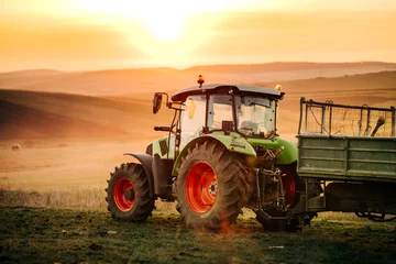 Foto auf Acrylglas Traktor Details des Landwirts, der auf den Feldern mit Traktor auf Sonnenuntergangshintergrund arbeitet. Details der Landwirtschaftsbranche