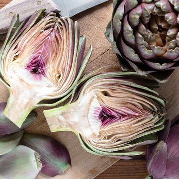 carciofi violetti interi e tagliati su tagliere di legno e coltello