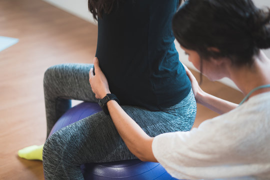 Pregnant woman pilates exercise workout at gym with personal trainer. Happy future mother doing pilates exercises