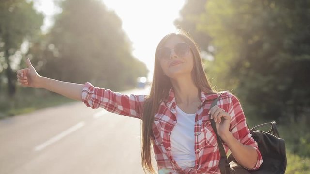 Traveler young woman hitchhiking on a sunny road. Young sexy girl looking for a ride to start a journey. Summer time