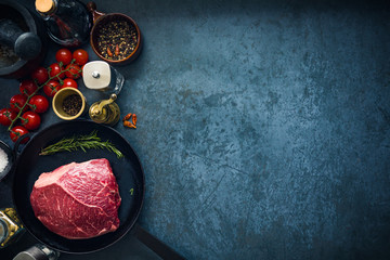 Raw marbled beef steak on cast iron pan with salt and herbs and tomatoes. Top view and copyspace.