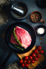 Raw Fresh Marbled Meat Beef on a cast iron pan ready for cooking on a blue concrete background top view.