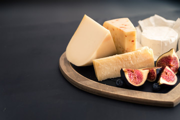 various types of cheese on rustic wooden table, goat cheese, chevre, grana padana, fig, blueberry