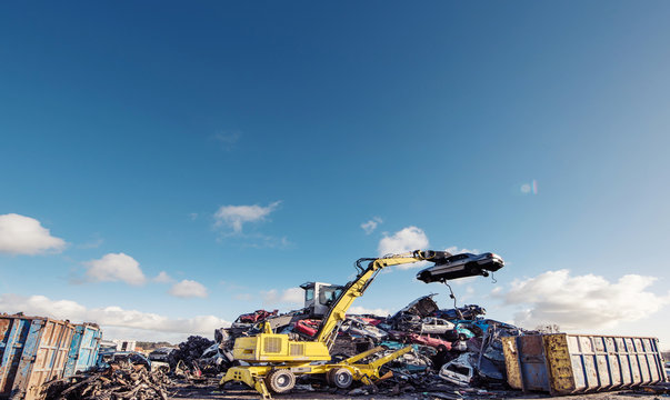 Yellow crane holding crashed car on scrapyard