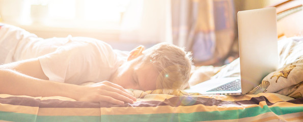 young person lying and sleeping on the bed in the sunny morning after working on laptop in the...