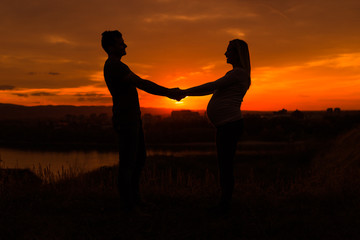 Fototapeta na wymiar Silhouettes of husband and pregnant wife holding hand and enjoy spending time together outdoor.