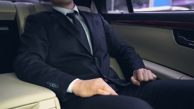 Businessman riding on backseat in luxury car, late for meeting, time management
