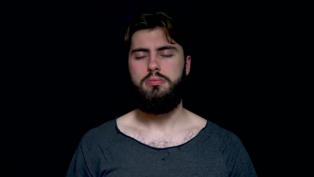 Portrait of disappointed, upset man with beard who covers his face with palm, isolated on black background. Disappointed, stressed out male in grey shirt making facepalm with hand