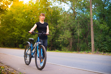 Naklejka premium young beautiful girl leads the bike on the sidewalk