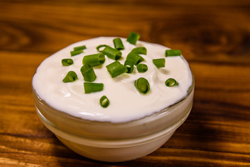 Glass bowl with sour cream and chopped green onion on wooden table