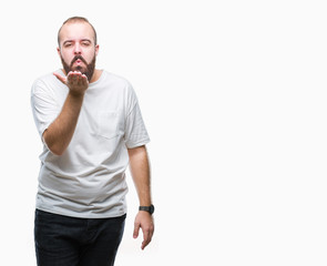Young caucasian hipster man wearing casual t-shirt over isolated background looking at the camera blowing a kiss with hand on air being lovely and sexy. Love expression.